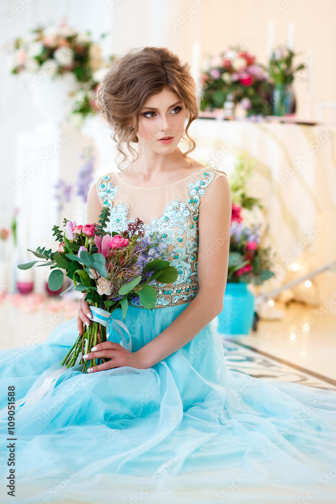 Beautiful young lady in a luxury blue dress in elegant interior with a bouquet of flowers Beautiful young lady in a luxury blue dress in elegant interior with a bouquet of flowers