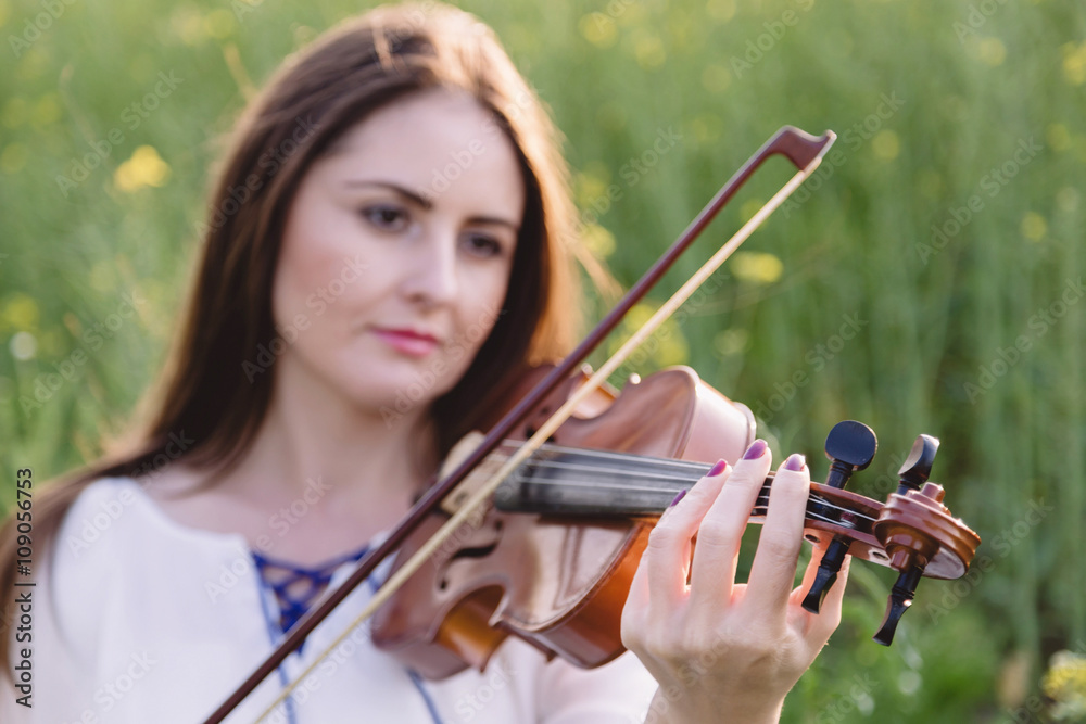 Young woman playing violin in a green field. Focus on the han Young woman playing violin in a green field. Focus on the han