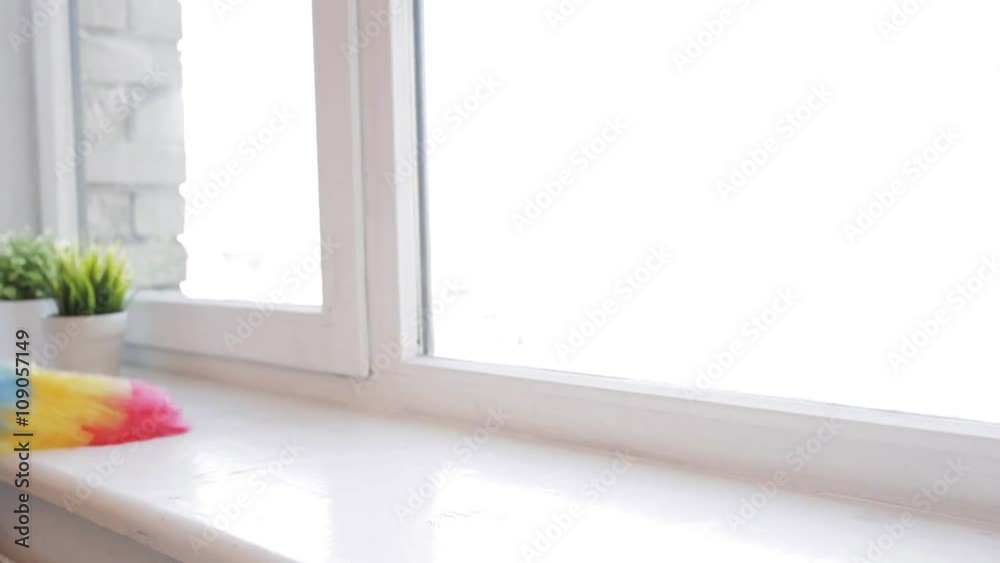 woman with duster cleaning window sill at home woman with duster cleaning window sill at home
