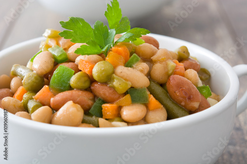 White beans with vegetables in a bowl on wood