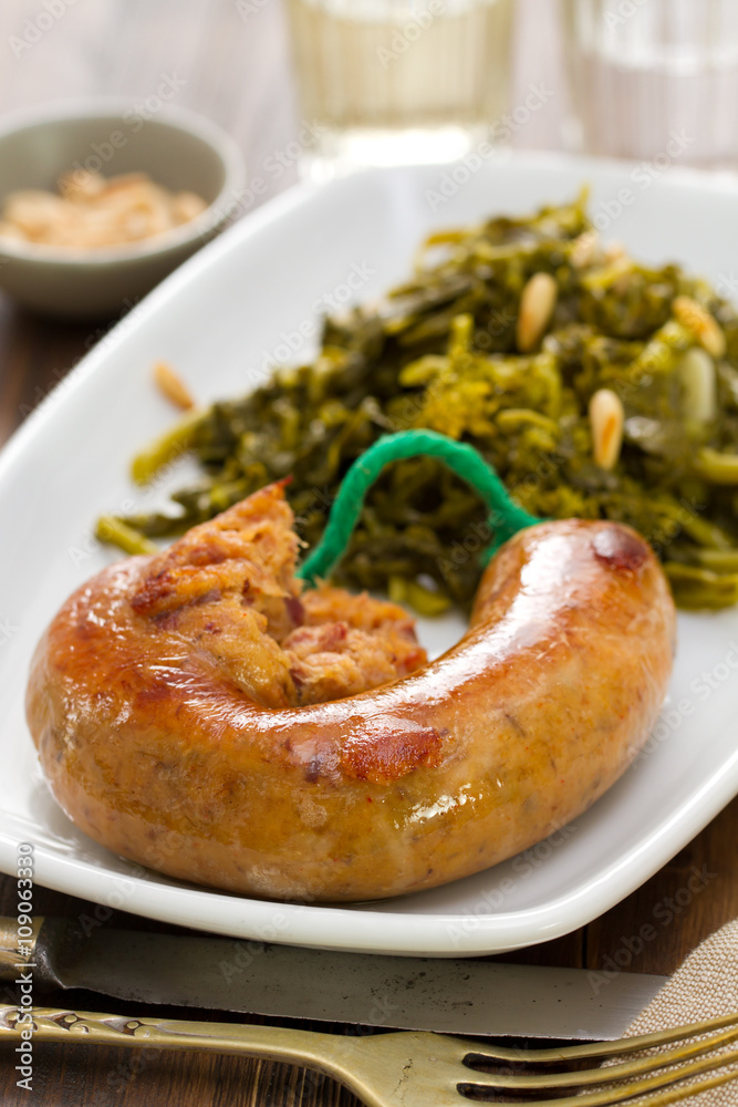 traditional portuguese smoked sausage with turnip greens on white plate on brown background