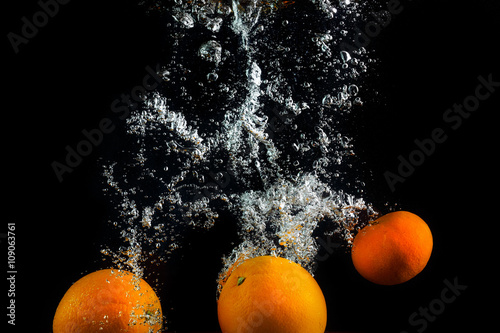 Fresh oranges and tangerines splash in water with air bubbles. Oranges in water on a black background. Healthy food. Wash fruits.