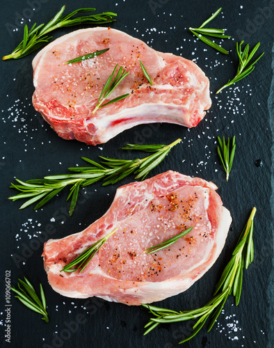Foto Raw pork steaks with rosemary on black stone background.