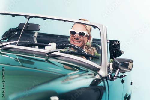 Smiling retro 1960s fashion woman with shades driving convertibl