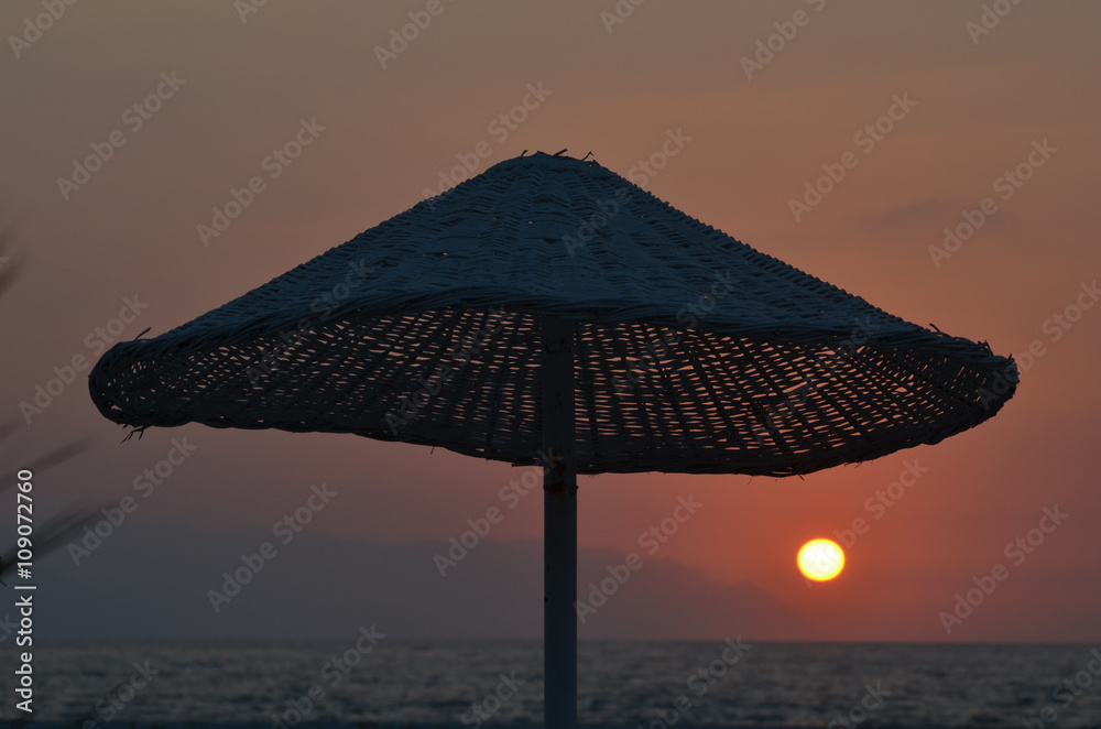 Reed parasol at sunset on the beach of the Mediterranean Sea, Kusadasi, Turkish Riviera, Turkey