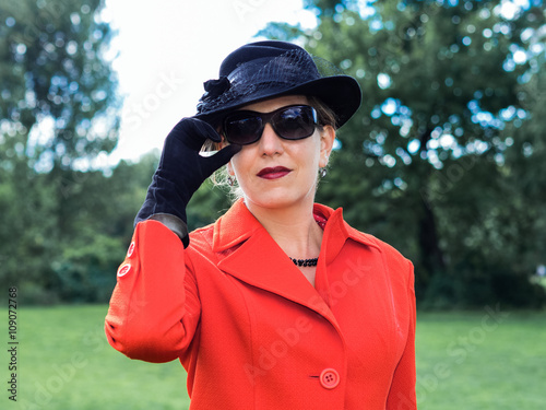 Attraktive Frau in einem rotem Kostüm mi Hut und Sonnenbrille -
