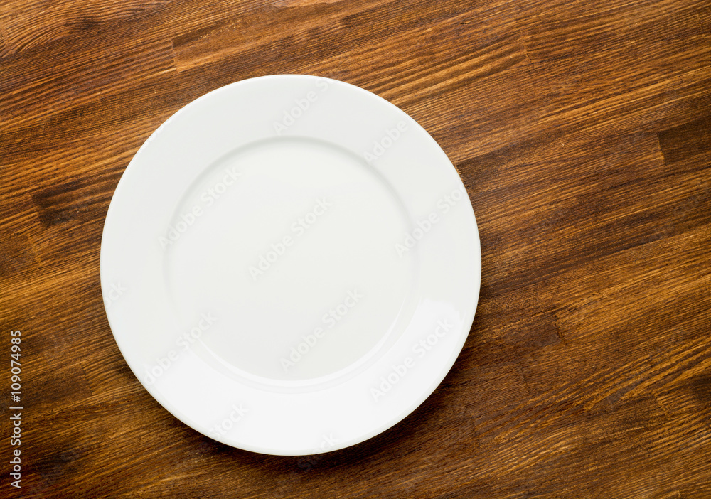 Empty white plate on wooden table top view Empty white plate on wooden table top view