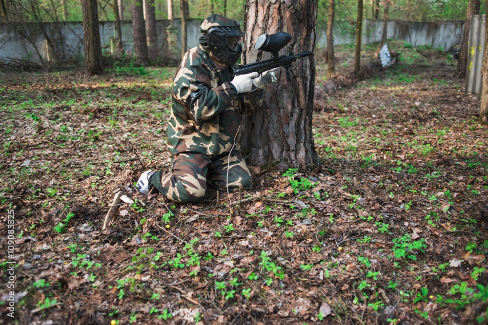 Man in a protective mask with a gun to play paintball in the woods in summer