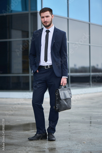 Fotografía Portrait of a guy in a suit with a briefcase in hand on background of the buildi