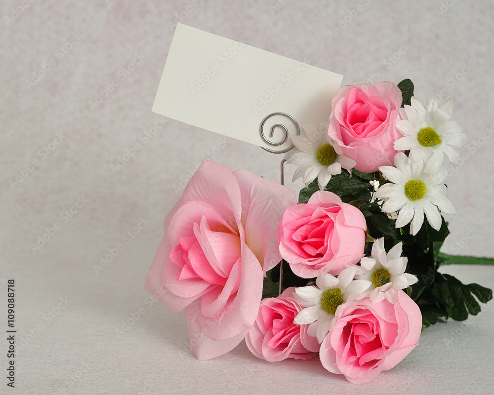 A bunch of artificial flowers with a blank note card displayed on a white background