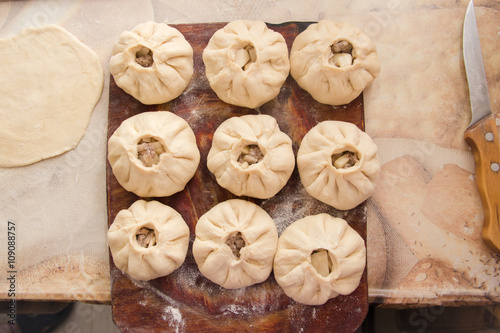 Vak belyash - homemade meat pies on woden chopping board frosted with flour, near  bread knife and pastry on table photo