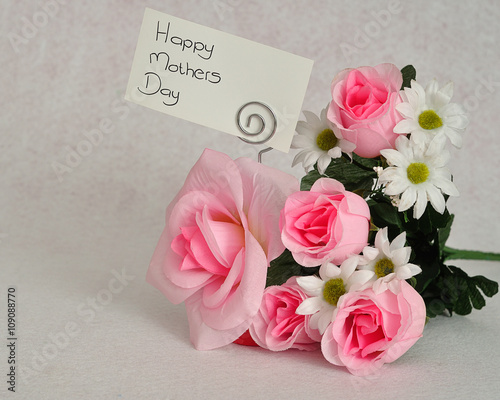 A bunch of artificial flowers with a card for happy mothers day isolated on a white background