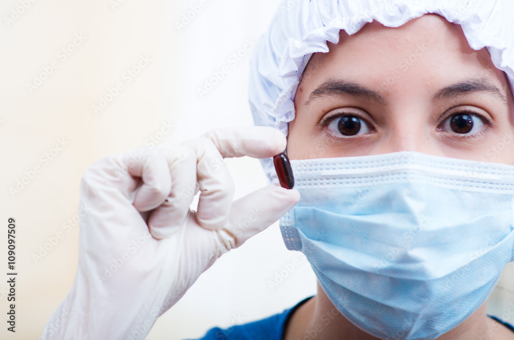 Closeup headshot nurse wearing bouffant cap and facial mask holding up two pill capsules for camera Closeup headshot nurse wearing bouffant cap and facial mask holding up two pill capsules for camera