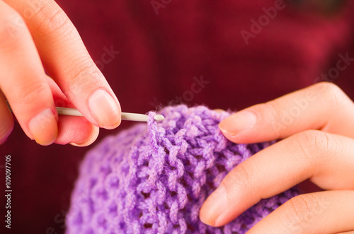 Closeup womans hands holding wooden knitting needles working on purple scarf
