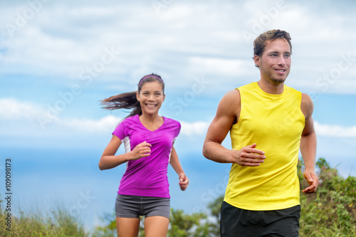 Healthy sports people trail running living an active life. Happy lifestyle couple of athletes training cardio together in summer outdoors. Multi-ethnic group Asian woman with handsome fit man trainer.