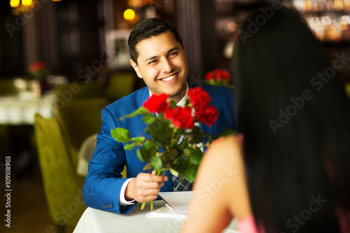 close-up of a man giving flowers to a woman on a date in a restaurant
