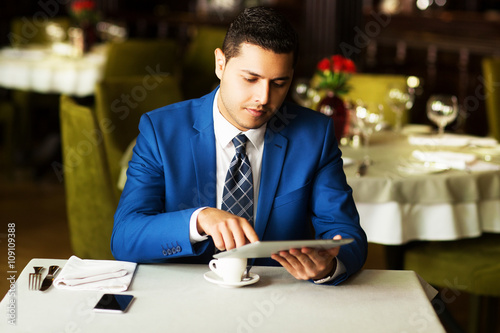 morning coffee, a young businessman with the tablet in a restaurant.young handsome businessman drinking coffee in a restaurant