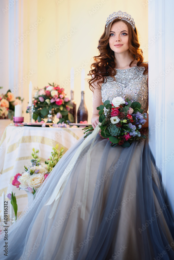 Beautiful young lady in a luxury dress in elegant interior with a bouquet of flowers