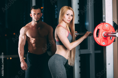 Young couple exercising in gym with weights man seems to be the personal trainer