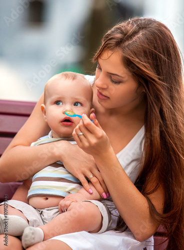 Portrait of happy beautiful mother feed her baby summer outdoors in park. Healthy child food for baby. photo