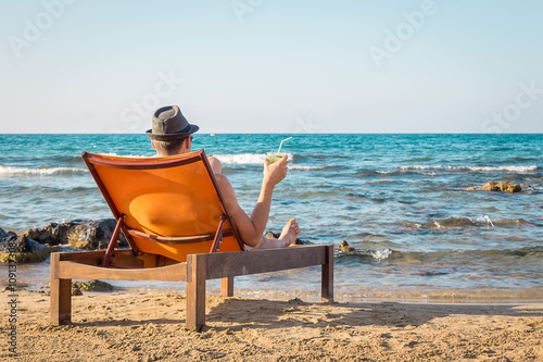 Young Man Relaxing on Chair Near the Sea and Drinking Cocktail Mojito