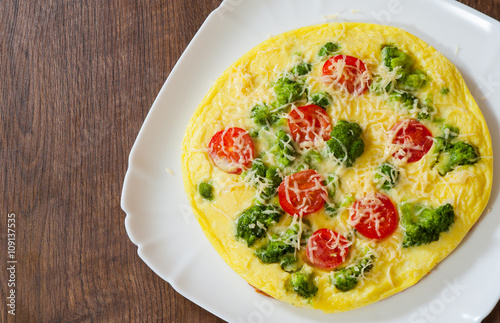omelet with tomato, broccoli and cheese in a plate on wooden table