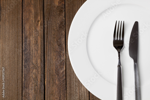 Fork and knife with white plate on dark wooden background  epty space on left