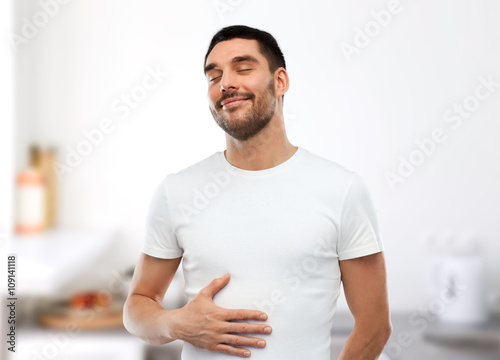 happy full man touching tummy over kitchen