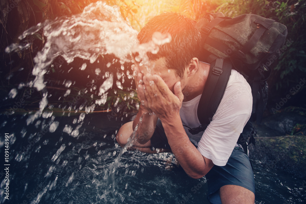 Fototapeta premium Young traveler washing his face in the wild river (intentional sun glare and motion blur)