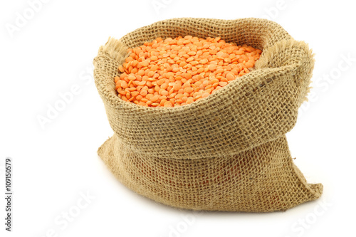 red lentils in a burlap bag on a white background