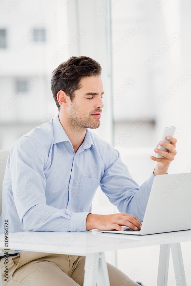 Businessman text messaging on phone while using a laptop Businessman text messaging on phone while using a laptop