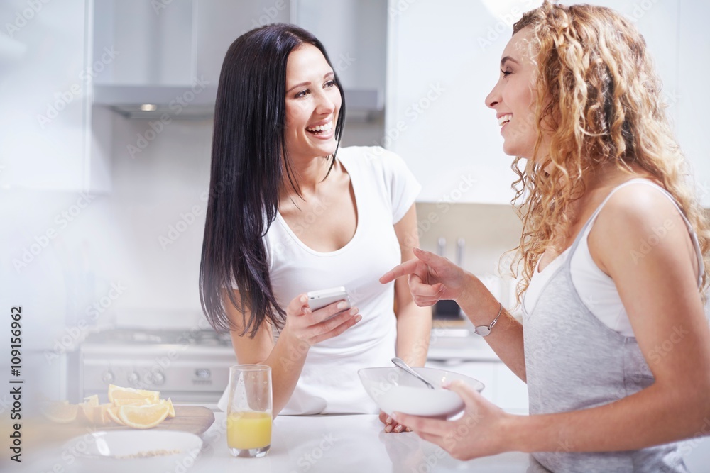 Two young female friends laughing at kitchen counter Two young female friends laughing at kitchen counter