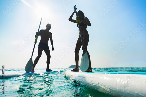 Stand up paddle board couple paddleboarding . Young caucasian couple on Thailand beach on summer holidays vacation travel.