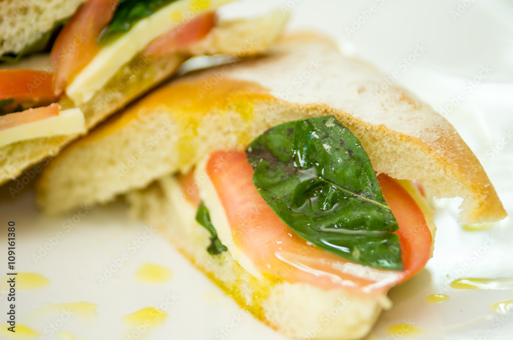 Obraz premium Delicious cheese, albahaca basil and tomato ciabatta sandwich on white plate