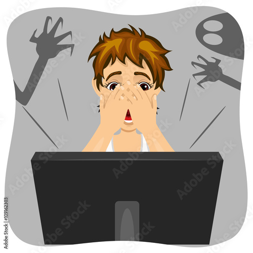 boy covering his face while watching horror movie on internet.  Shadow of ghost is on wall