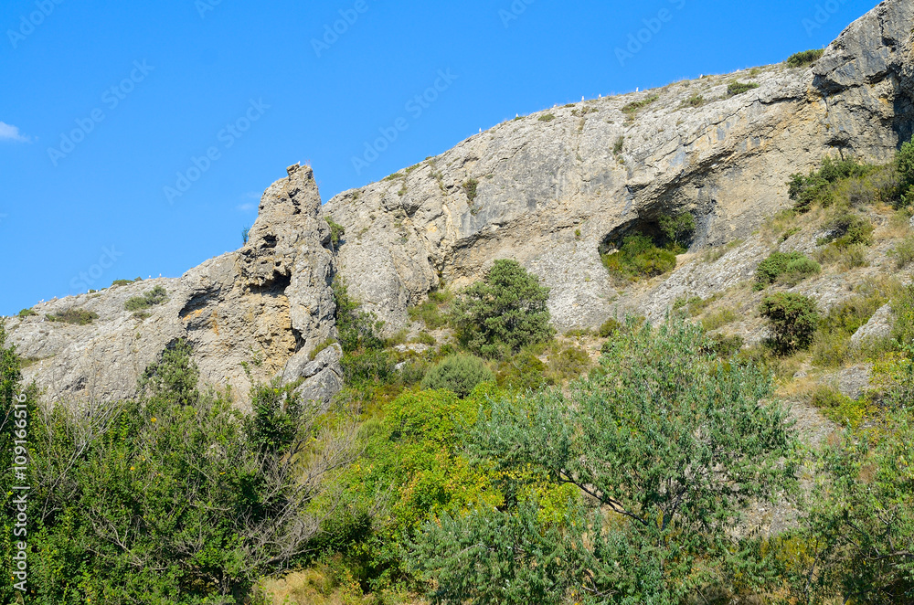 Mountain landscape with sparse greenery. Caves. Roast hot summer. Blue sky.