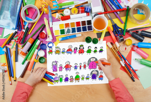 child drawing cute happy cartoon people in row, top view hands with pencil painting picture on paper, artwork workplace