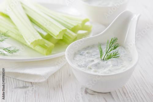 Fresh celery sticks with yogurt dip on white wooden background