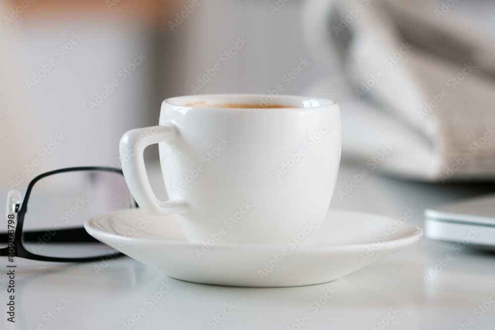Close up view of white coffee cup on table with glasses and news