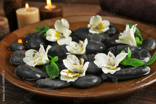 Spa wooden bowl with water  flowers and stones closeup