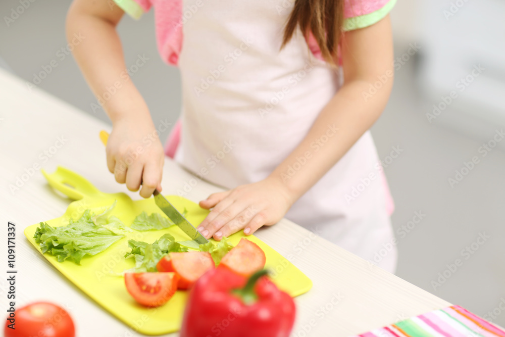 Little girl's hands cutting vegetables on a board. Little girl's hands cutting vegetables on a board.