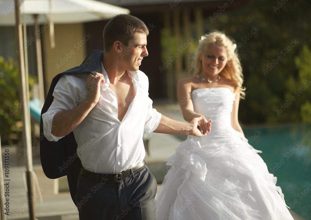 Lovely bride and groom coming across pool area after wedding.