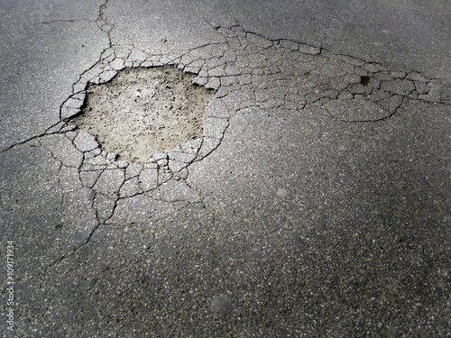 Cracked damaged asphalt street with a big hole