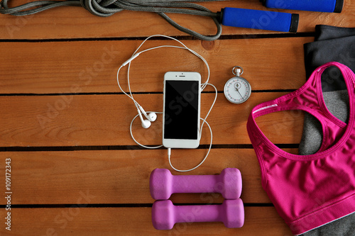 Sport equipment and clothes with mobile phone on wooden background