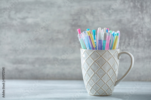 Pens in ceramic cup on grey background