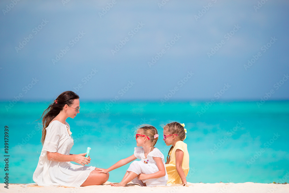 Young mother applying sunscreen on her kids at the beach Young mother applying sunscreen on her kids at the beach