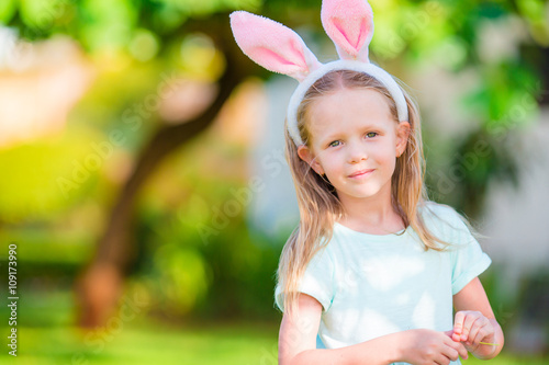 Adorable little girl wearing bunny ears with Easter eggs on spring day