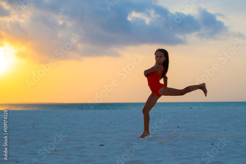 Silhouette of adorable active little girl on white beach at sunset