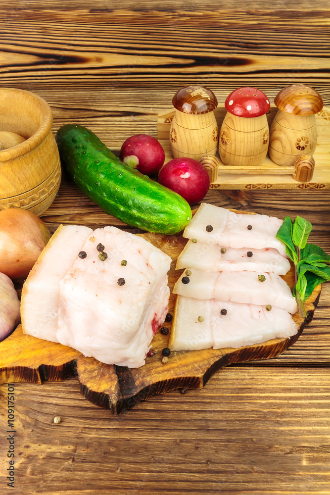 Piece and sliced fresh, raw pork lard on wooden board with vegetables, spices on the table. Piece and sliced fresh, raw pork lard on wooden board with vegetables, spices on the table.