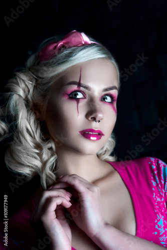 Beautiful blonde girl with two pigtails, with creative doll make-up: pink glossy lips, wearing pink skeleton dress. for the Halloween party. Close up, retouched image.